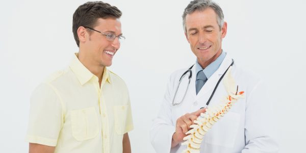 Smiling male doctor showing patient something on skeleton model over white background